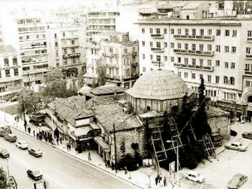 Φωτογραφία του 1980, στην οποία διακρίνονται τα καταστήματα, η ταμπέλα του κινηματογράφου, αλλά και κάποιες απόπειρες στήριξης του μνημείου