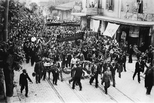 Στιγμιότυπο από ομάδες μελών σωματείων που διαδηλώνουν σε κεντρικούς δρόμους της μακεδονικής μεγαλούπολης. Στις πρώτες γραμμές κρατούν μεγάλα ανθοστόλιστα στεφάνια του Μάη
