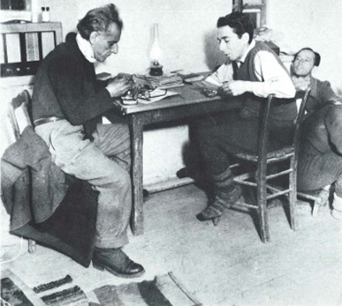 Χειμώνας 1948. Ο Αντώνης Γιαννίδης στην έδρα του Καλλιτεχνικού Συγκροτήματος του Γενικού Αρχηγείου, στο χωριό Πυξός, κοντά στην Πρέσπα. Στρίβει τσιγάρο, ενώ ακούει τον Δημήτρη Ραβάνη-Ρεντή να διαβάζει μια σκηνή από θεατρικό του. Ο τρίτος δεξιά είναι ο πρώην αστυφύλακας Γιώργος Κοσκινάς, ηθοποιός, τραγουδιστής και μαχητής που σκοτώθηκε στο Βίτσι (Αρχείο Περιοδικού «Θέατρο»)