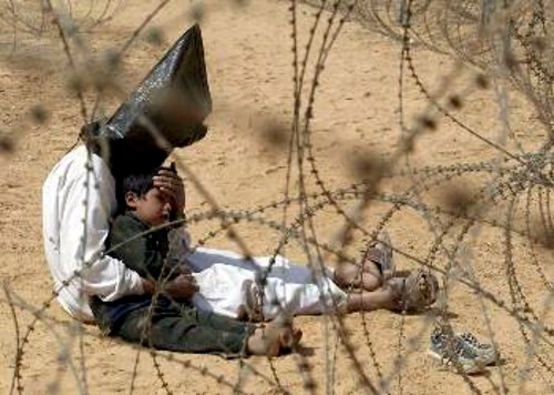 Με κουκούλα στο κεφάλι και το γιο του αγκαλιά σε κάποιο αμερικανικό στρατόπεδο συγκέντρωσης. Φωτογραφία-σύμβολο της «απελευθέρωσης» του Ιράκ