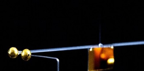 Αριστερά το χρυσό σφαιρίδιο ελέγχου στερεωμένο στη μια άκρη του εκκρεμούς στρέψης και λίγο δεξιότερα το σφαιρίδιο - «πηγή» της βαρυτικής έλξης. Λίγο δεξιά από το μέσον της φωτογραφίας, ίσα ίσα διακρίνεται το λεπτότατο νήμα από το οποίο κρέμεται το εκκρεμές