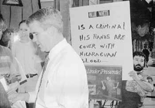 Ο Ολιβερ Νόρθ, υποψήφιος γερουσιαστής μιλάει με ψηφοφόρους τους τον Οκτώβρη του 1994. Πίσω του ένας διαδηλώτης κρατάει πλακάτ με το σύνθημα: «Είναι εγκληματίας. Τα χέρια του είναι βαμένα με νικαραγουανό αίμα».