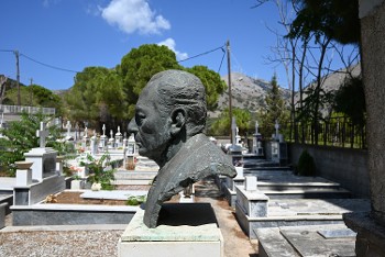 Η προτομή του Γεράσιμου Παπαδάτου σε προφίλ, με τον χρόνο σταματημένο στο απόμερο νεκροταφείο των Φαρακλάτων, μοιάζει να αποτελεί μια εμβληματική φιγούρα μέσα στο θλιμμένο τοπίο του κοιμητηρίου, ενώ στο βάθος η σύγχρονη «πράσινη» Ενέργεια στεφανώνει τις κορυφογραμμές του τοπίου
