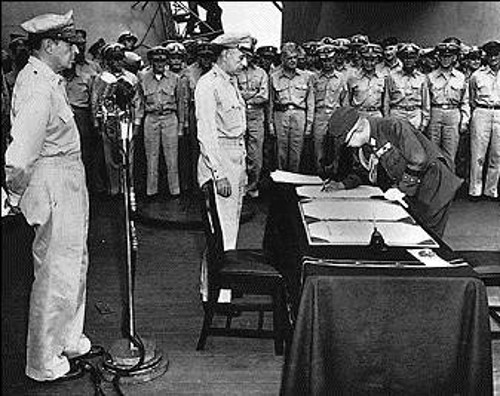 Η Ιαπωνία συνθηκολογεί άνευ όρων και σταματά κάθε πολεμική δραστηριότητα. Ο Αμερικανός αρχιστράτηγος Ντάγκλας Μακ Αρθουρ (όρθιος δίπλα στην καρέκλα). Ο αρχηγός του Γενικού Επιτελείου της Ιαπωνίας στρατηγός Γιοσιτζίρο Ουμάτζου (εδώ υπογράφει) ως εκπρόσωπος των ενόπλων δυνάμεων της χώρας