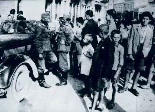 Κατά την κατάληψη της Κρήτης, σε δρόμο του Ηρακλείου Γερμανοί στρατιώτες. Τα παιδιά κακοντυμένα, ξυπόλυτα και πεινασμένα τους χαζεύουν