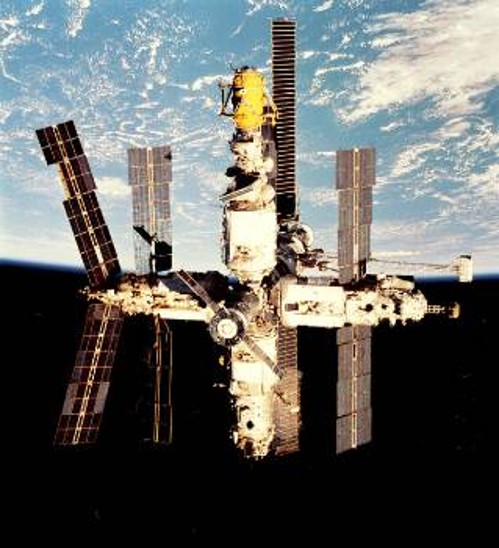 Εντυπωσιακή φωτογραφία του «ΜΙΡ» με φόντο τη Γη και το αχανές Διάστημα. Σε πρώτο πλάνο διακρίνεται ένα διαστημόπλοιο «Σογιούζ», που έχει προσδεθεί στο σταθμό