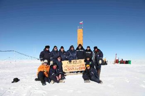 Η ρωσική ομάδα επιστημόνων φωτογραφίζεται με πινακίδα που γράφει την ημερομηνία και το ακριβές βάθος, όπου το γεωτρύπανο συνάντησε την επιφάνεια της υποπαγετωνικής λίμνης Βοστόκ. Πίσω τους φαίνεται η κορυφή της εγκατάστασης του γεωτρύπανου