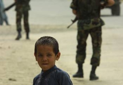 Ενας μικρός Αφγανός κοιτά το φακό, ενώ, στο φόντο, στρατιώτες της διεθνούς δύναμης «ασφάλειας» περιπολούν με το δάχτυλο στη σκανδάλη...