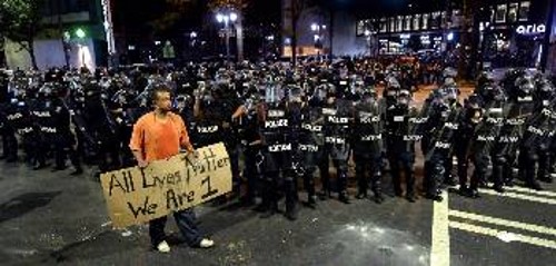 «Ολες οι ζωές μετράνε! Είμαστε ένα», γράφει το πλακάτ του διαδηλωτή με φόντο δεκάδες πάνοπλους αστυνομικούς