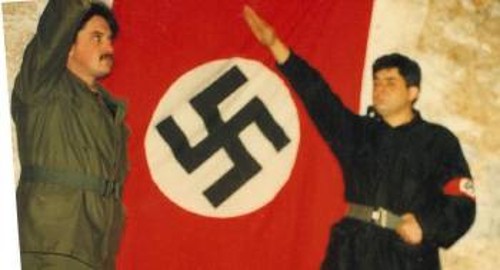 Ναζιστικοί χαιρετισμοί του αρχηγού Μιχαλολιάκου και του υπαρχηγού Παππά, με φόντο τη σβάστικα