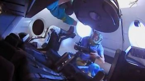 Δύο μέλη του πληρώματος του ΔΔΣ έχουν μπει στην κάψουλα του «Crew Dragon» (το ένα στην μπουκαπόρτα) λίγο μετά τη σύνδεσή του με το σταθμό, φορώντας προστατευτική μάσκα για να μην αναπνεύσουν τυχόν αιωρούμενα σωματίδια. Στο βάθος, με την άσπρη στολή της «SpaceX», μια κούκλα εξοπλισμένη με αισθητήρες, η οποία χρησιμοποιήθηκε για να καταγραφούν οι καταπονήσεις, που θα δεχόταν ένας άνθρωπος αν βρισκόταν μέσα στο σκάφος από την εκτόξευση έως την πρόσδεση